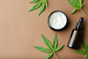Top view of Cannabis cosmetic oil cream in jar bottle and a green plant leaf